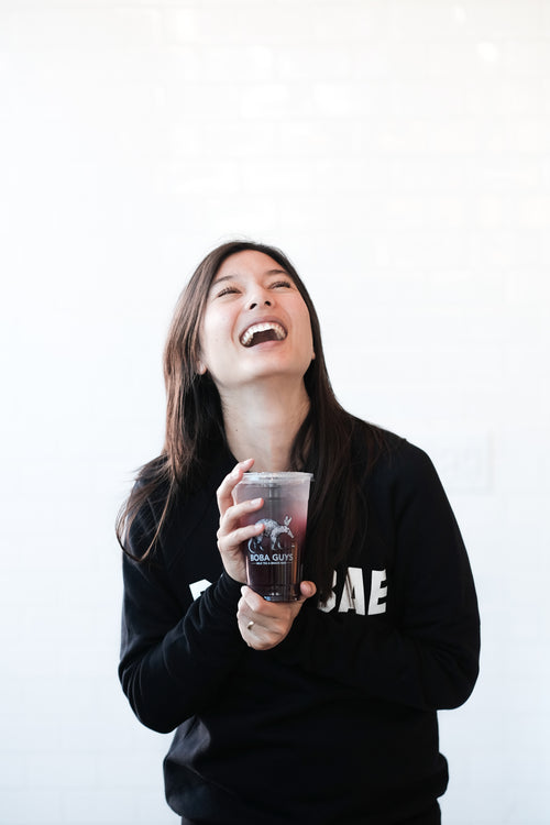 Woman laughing wearing a Boba Bae sweater and holding a boba drink