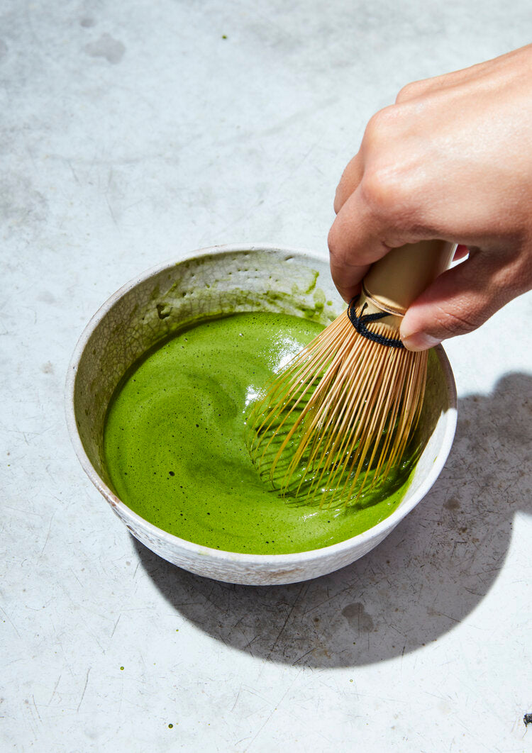 Hand whisking matcha in a bowl on concrete